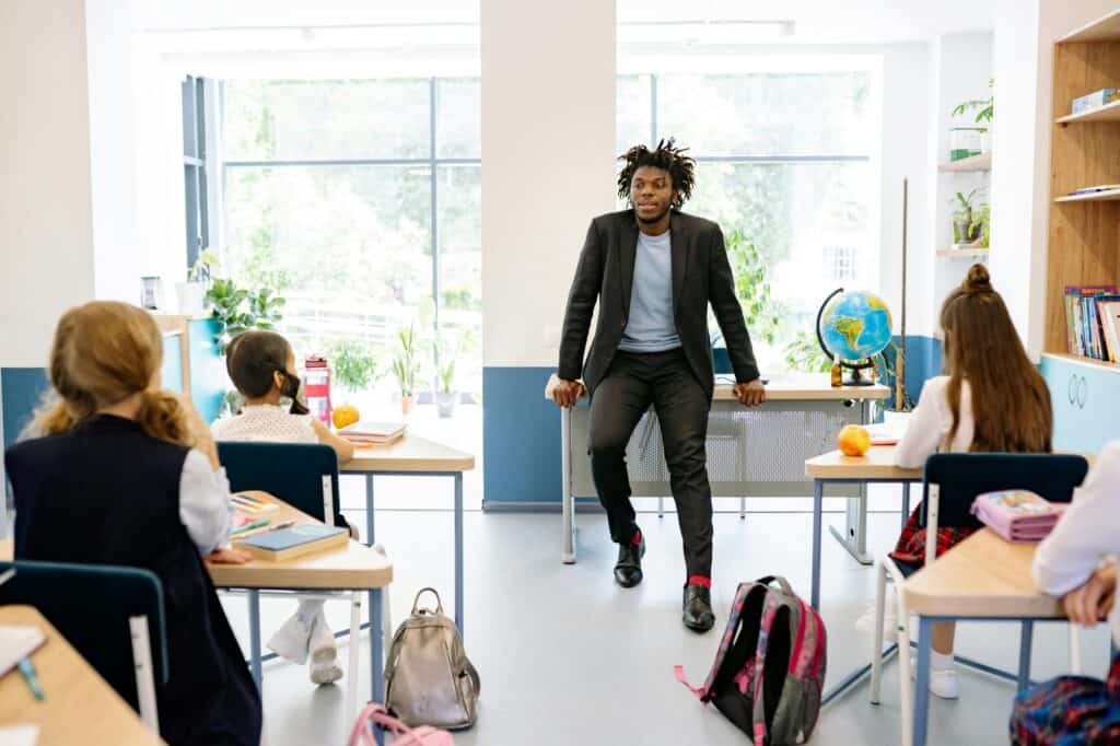 A teacher in front of a class and his students are paying attention to him